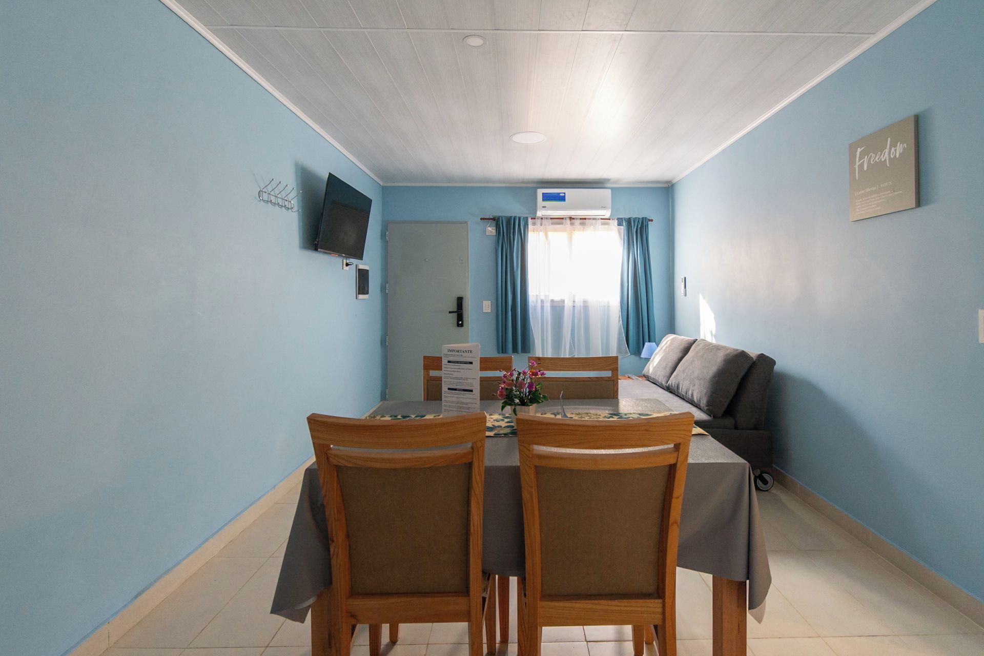 Un comedor con una mesa y sillas, un sofá, un televisor y un cartel con texto.