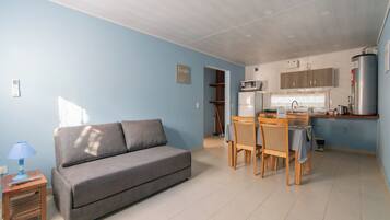 A compact living space with a sofa, dining table, chairs, a kitchen area with appliances, and a small side table.