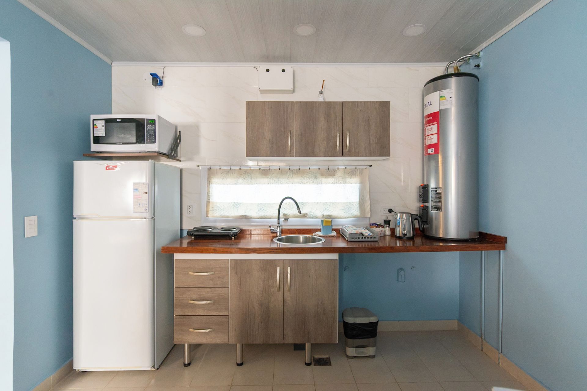 Una cocina compacta equipada con refrigerador, microondas, lavamanos y calentador de agua.