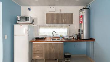 Una cocina compacta equipada con refrigerador, microondas, lavamanos y calentador de agua.