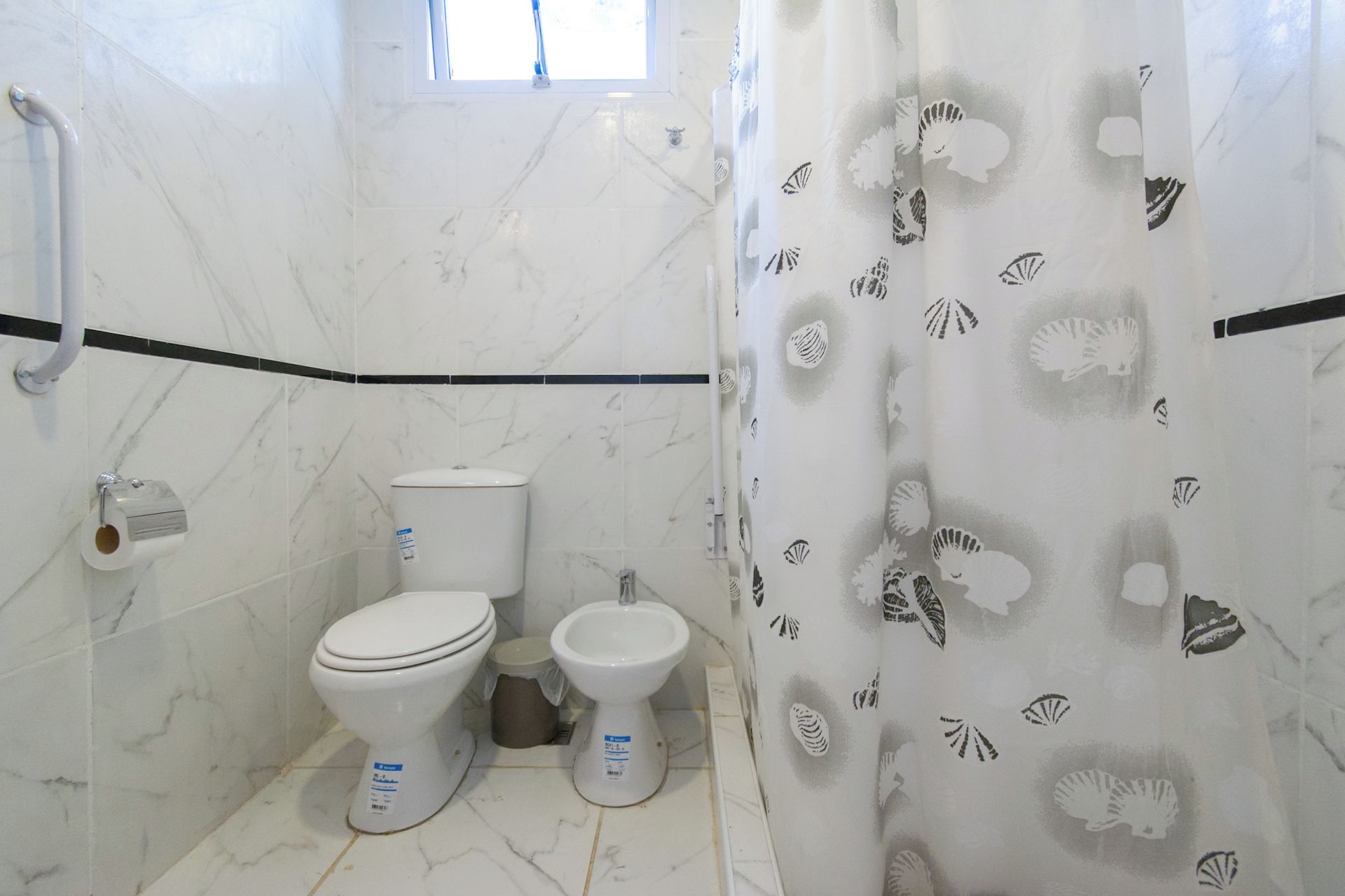 Un baño con dos inodoros, un bidé y una cortina de ducha con estampado de conchas.