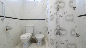 Un baño con dos inodoros, un bidé y una cortina de ducha con estampado de conchas.