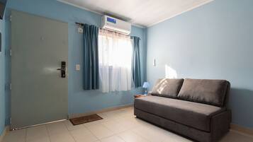 A room with a grey sofa, a door, and a window with curtains.