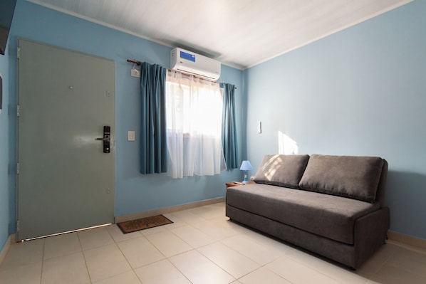 A room with a grey sofa, a door, and a window with curtains.