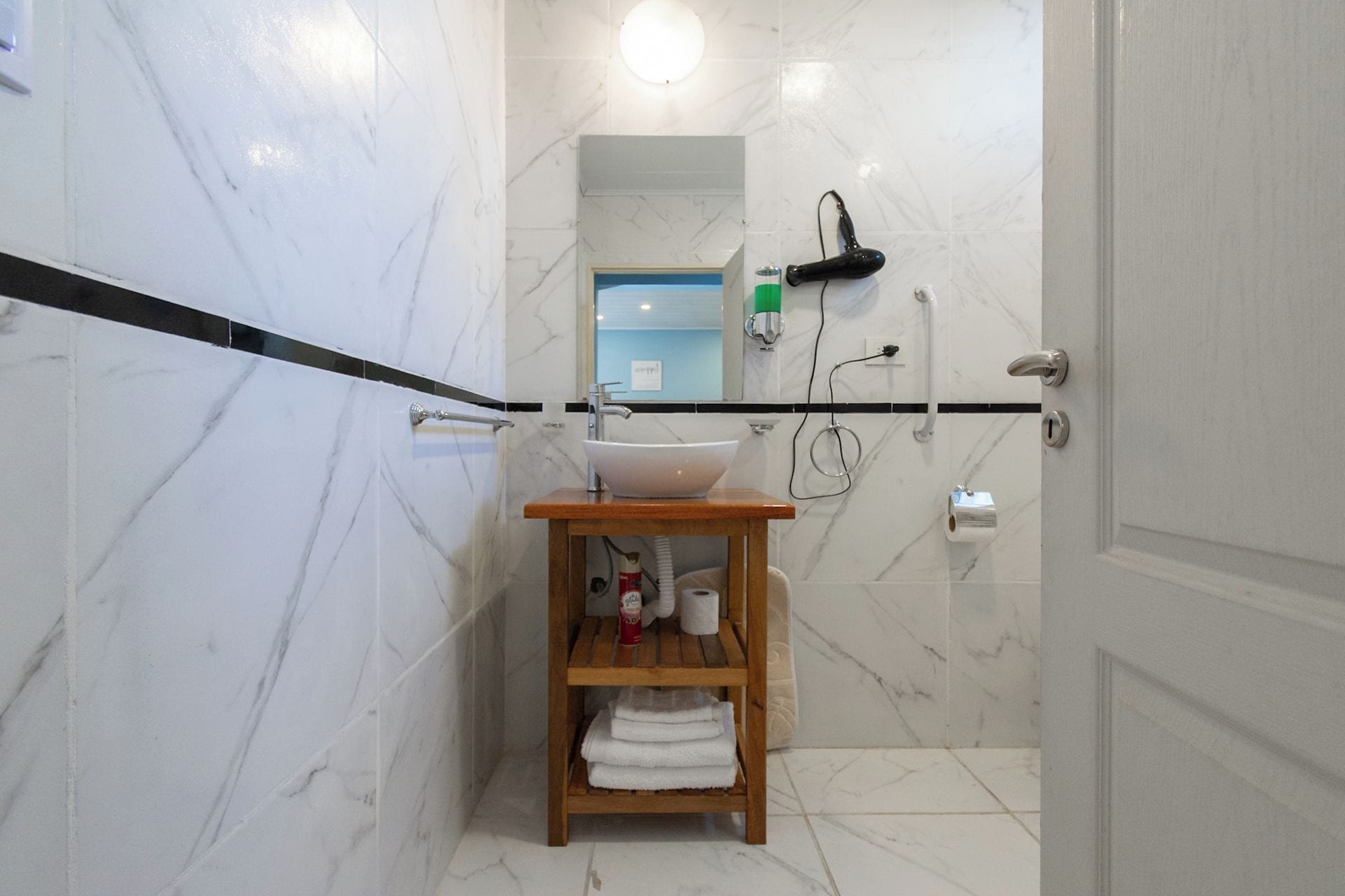 Un baño con piso de mármol, tocador de madera con lavamanos y un perchero.