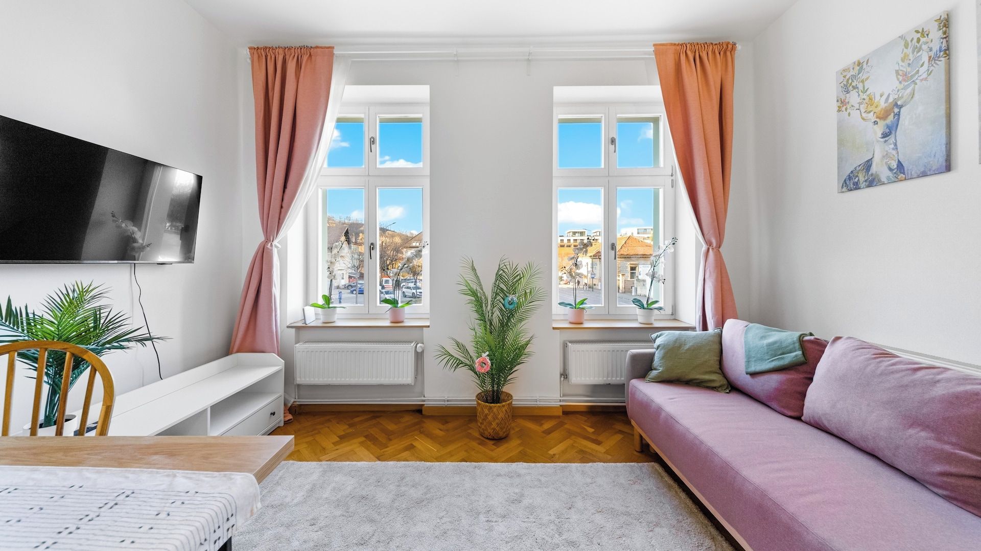 Un salon moderne avec un canapé, un téléviseur et une vue sur la ville grâce à de grandes fenêtres.