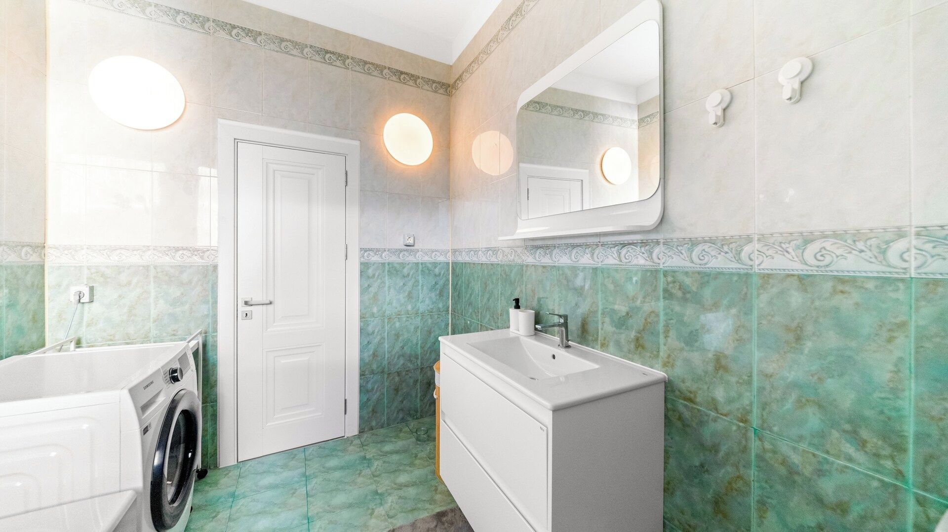 Ein Badezimmer mit einem weißen Waschbecken, einem Spiegel und einer Waschmaschine.