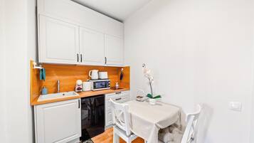 A compact kitchenette with white cabinets, a wooden countertop, a microwave, a kettle, and a small table with chairs.