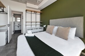 Ein modernes Schlafzimmer mit einem großen Bett, einem Kopfteil, einem Nachttisch und einem Spiegel.