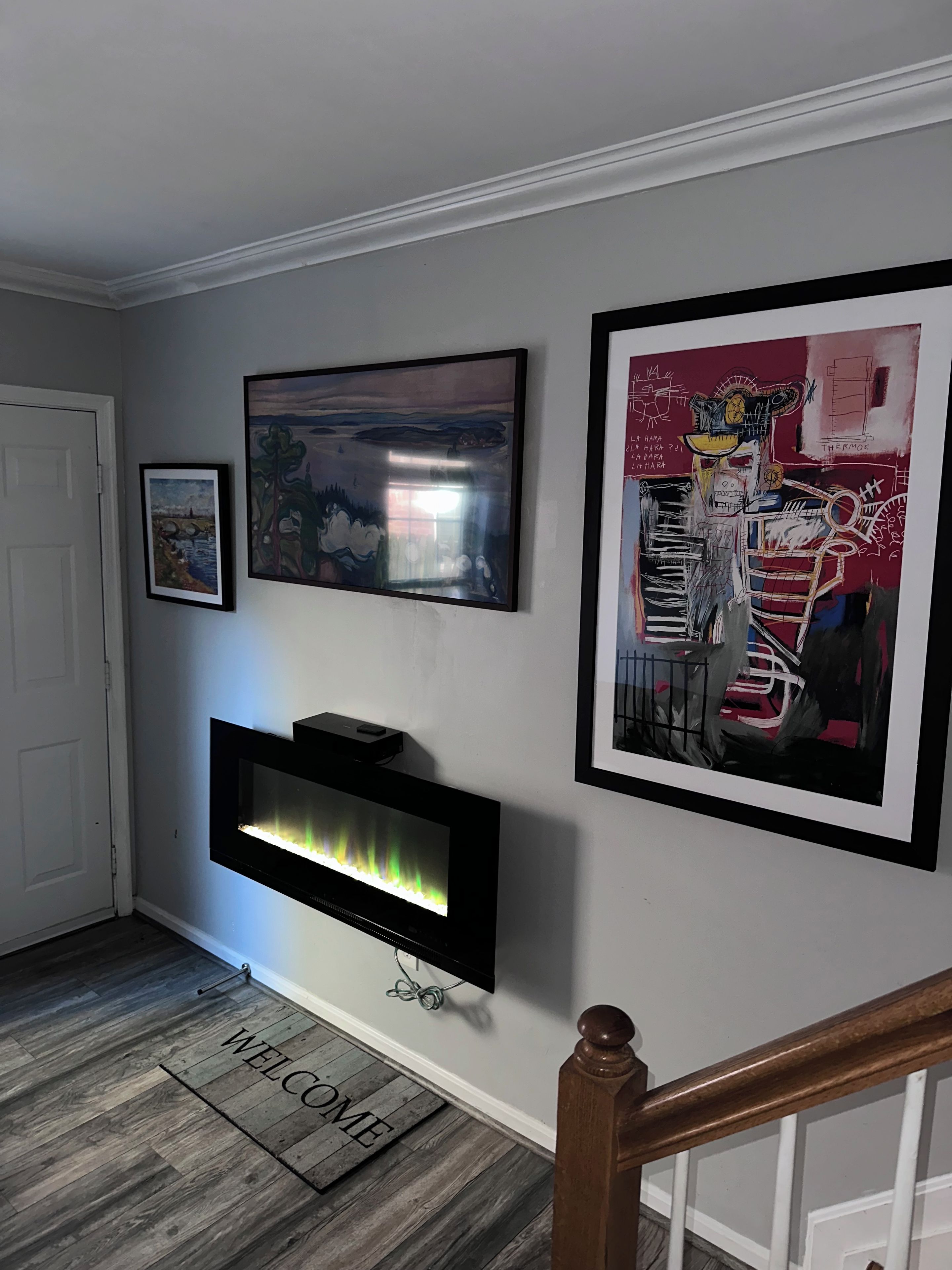 A hallway with a flat-screen TV mounted on the wall, a welcome mat, and framed artwork.