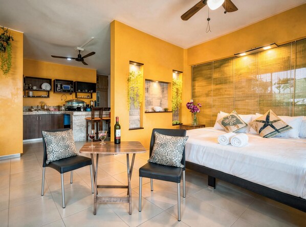 Quarto de hotel moderno com cama, duas cadeiras, mesa de jantar, cozinha e ventilador de teto.