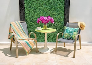 Two chairs with a table between them, a green wall with foliage, and a straw hat on one of the chairs. - King, Queen, Double Beds Sleep 8 Duplex, Kitchen, Wifi, AC, Free Bikes, Parking (Playa del Carmen)