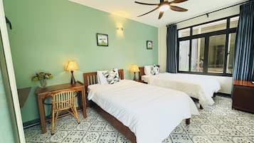 Une chambre d’hôtel avec deux lits, un bureau, une chaise, un ventilateur de plafond et une fenêtre avec des rideaux.