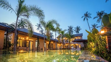 A resort with a swimming pool, palm trees, and multiple buildings with warm lighting.