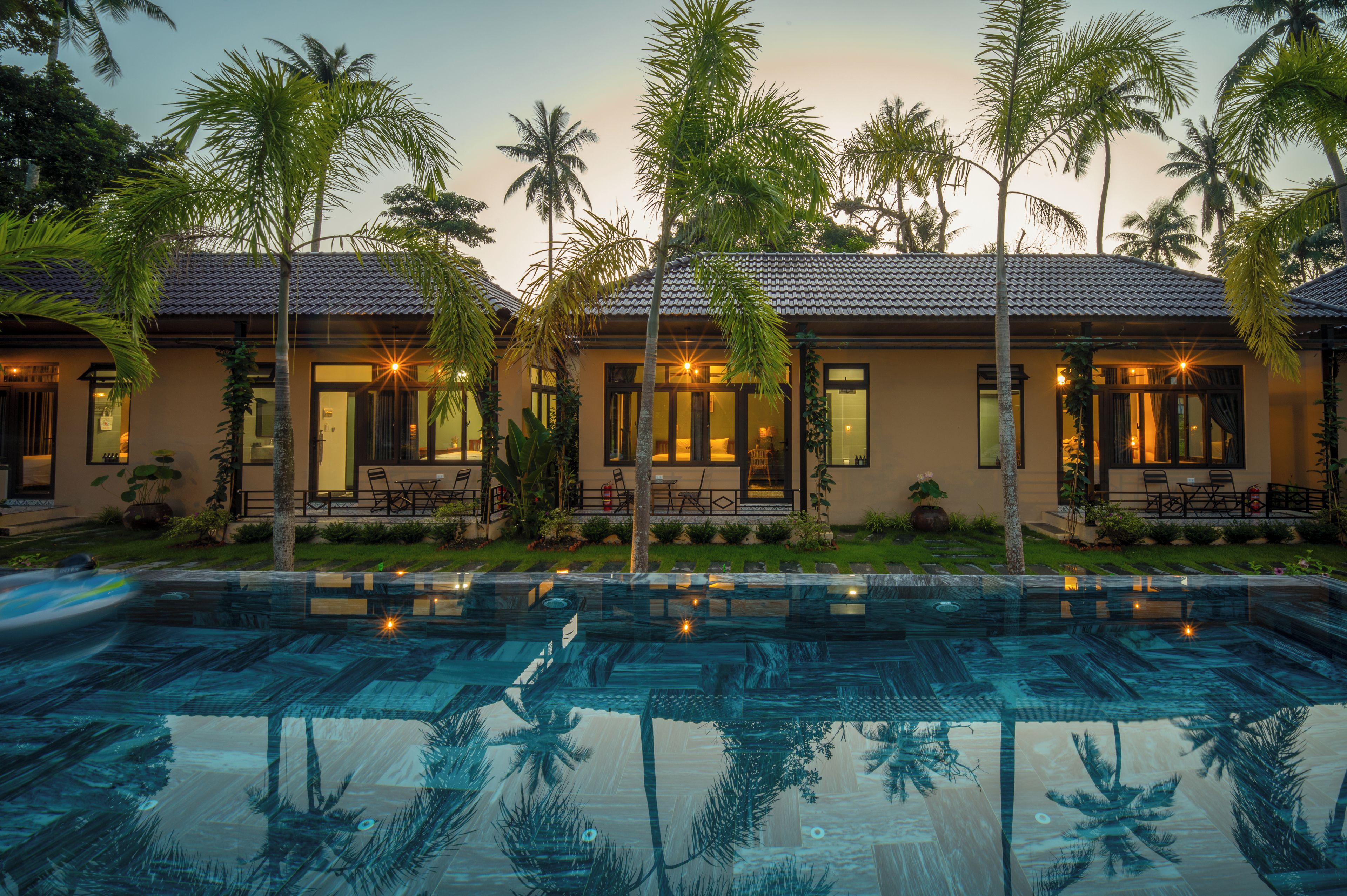 A resort with a swimming pool, palm trees, and a building with multiple rooms and a patio area.