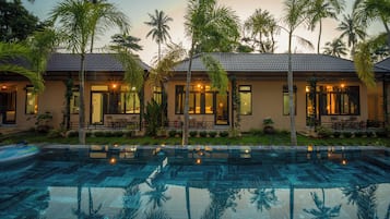 A resort with a swimming pool, palm trees, and a building with multiple rooms and a patio area.