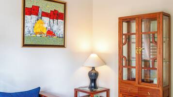Una habitación con un sofá azul, un mueble de madera con puertas de cristal, una mesa con lámpara y un suelo estampado.