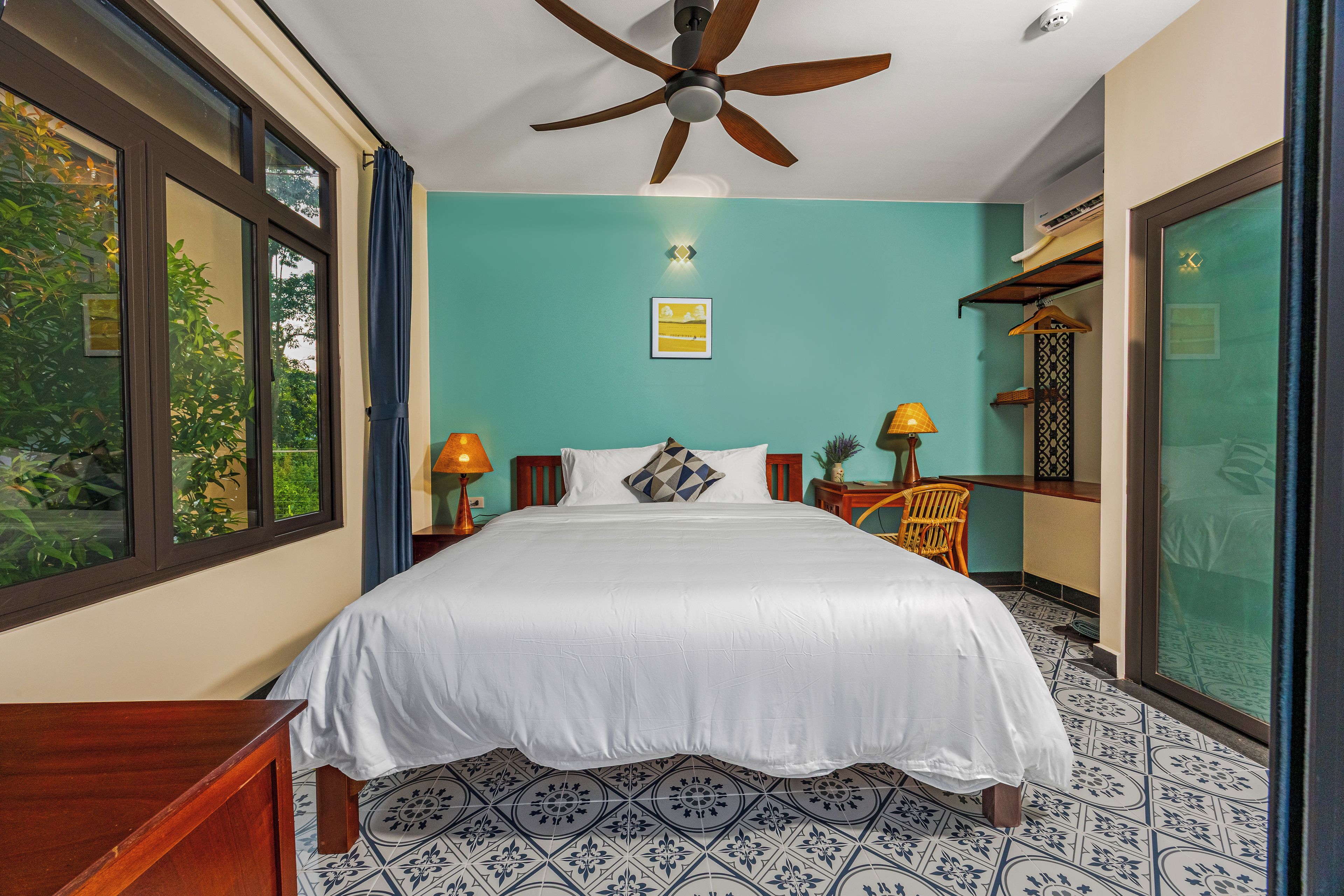 A bedroom with a bed, a ceiling fan, a window, and a view of greenery outside.