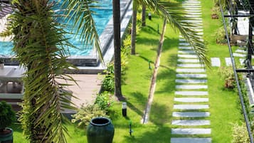 A pool area with a clear pathway leading to the pool, surrounded by greenery and palm trees.