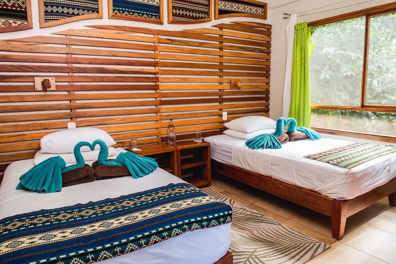 Una habitación con dos camas de madera, cabeceros de madera, una ventana con cortinas y una alfombra estampada.