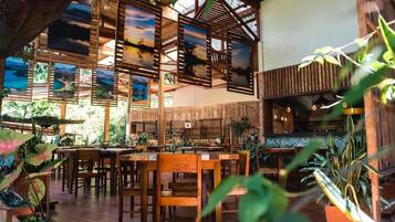 Un restaurante con mobiliario de madera, separadores de bambú y obras de arte en las paredes.