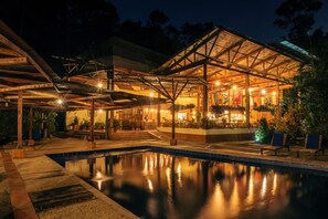 A poolside area with a covered seating area and a building with multiple levels and a roof structure.