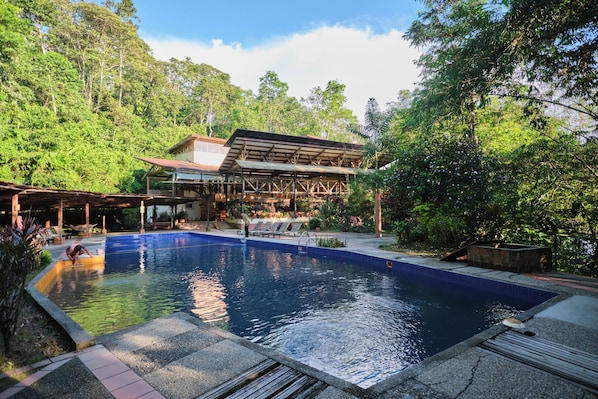 A swimming pool with a covered seating area and a building in the background.