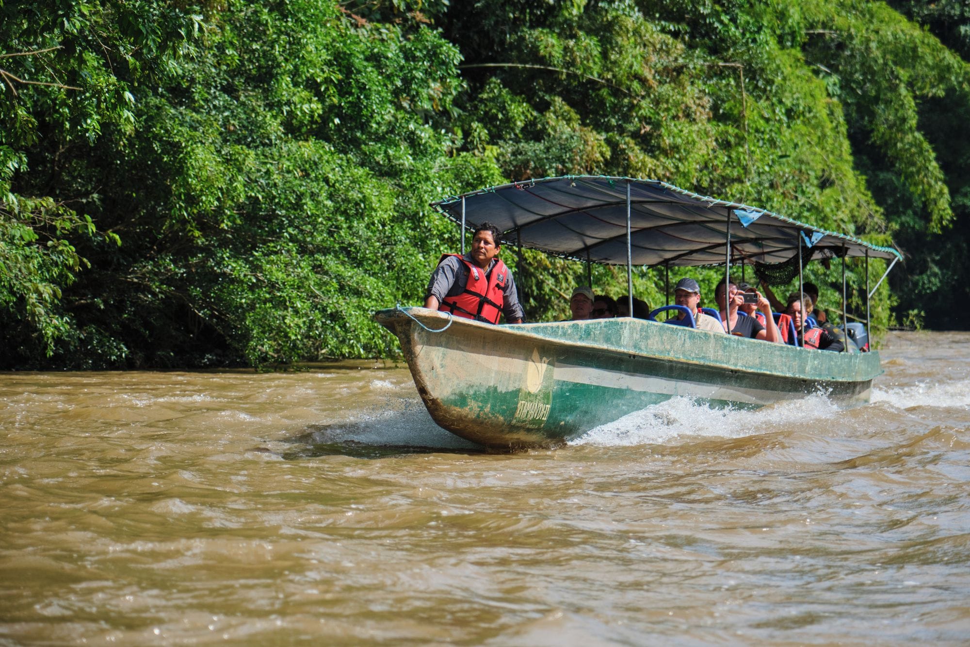 Un bateau transportant des passagers navigue sur une rivière bordée d’une végétation luxuriante.