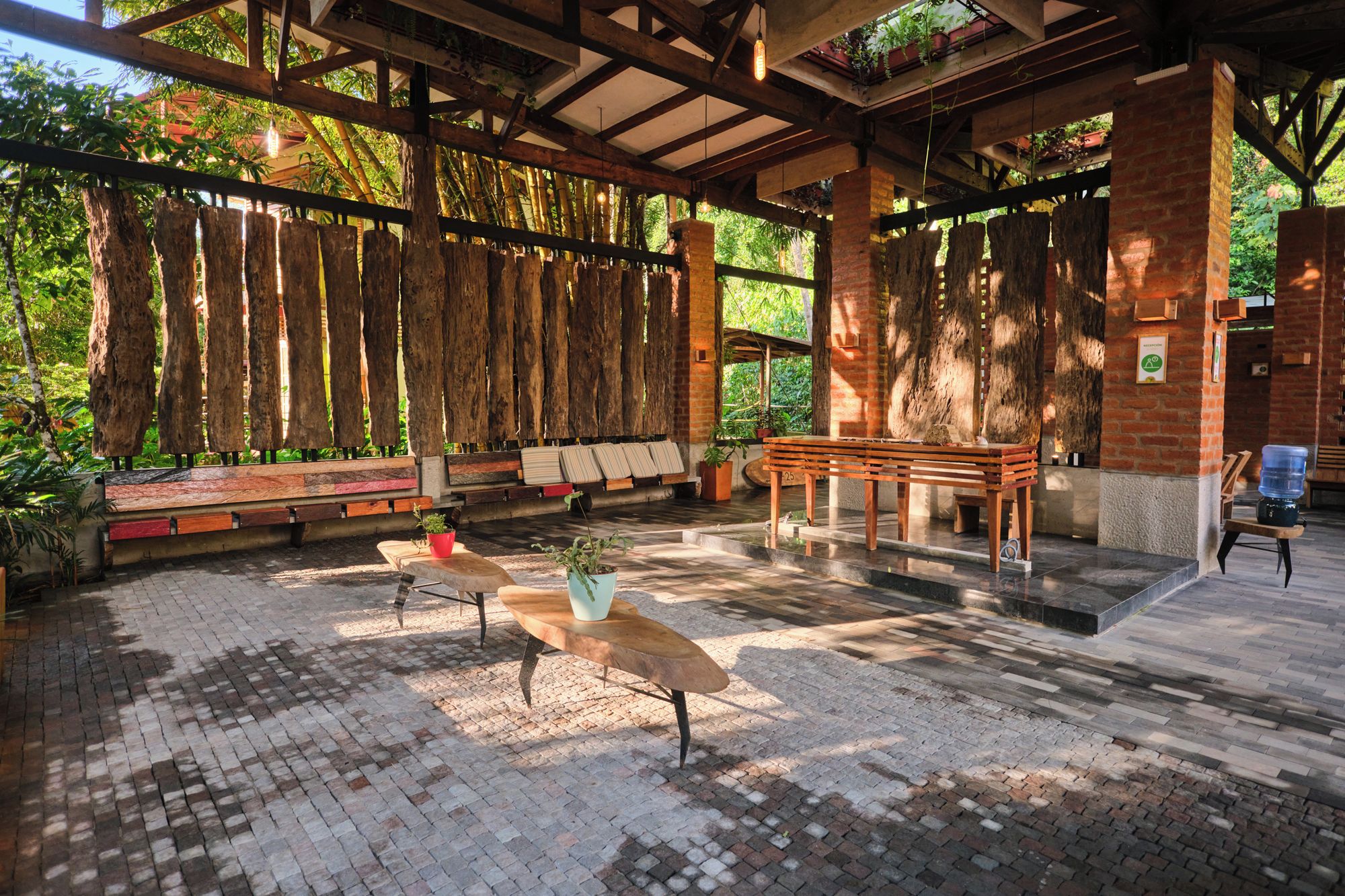 An outdoor patio area with a wooden bench, a table with a potted plant, and a water dispenser.