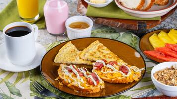Ein Frühstückstisch mit Toast, belegt mit Käse und Wurst, ein Glas Orangensaft, eine Tasse Kaffee und eine Schüssel Granola.