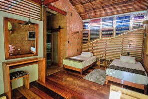 A room with two beds, a wooden bench, a mirror, and a wall with patterned textiles.