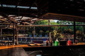 An outdoor seating area with tables and chairs, surrounded by glass walls, and a view of greenery.