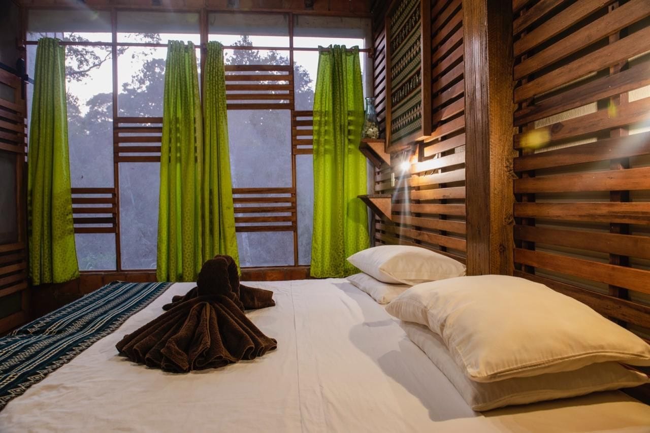 A room with a bed, green curtains, a wooden headboard, and a patterned rug.