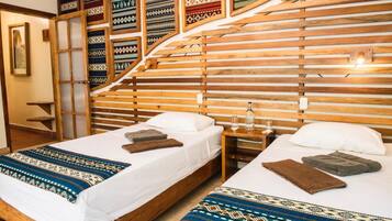 Habitación de hotel con dos camas, cabeceros de madera y una pared decorada con tejidos estampados.