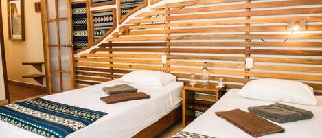 A hotel room with two beds, wooden headboards, and a wall decorated with patterned textiles.