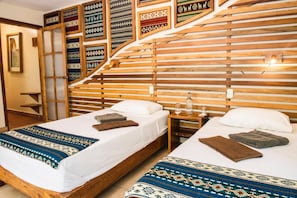 A hotel room with two beds, wooden headboards, and a wall decorated with patterned textiles.