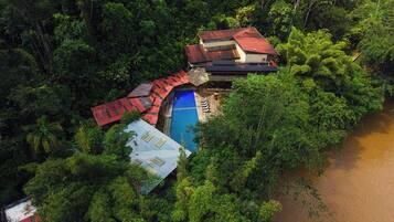 Ein abgelegenes Resort mit Swimmingpool, umgeben von dichtem Wald, einem kleinen Gebäude mit rotem Dach und einem Fluss in der Nähe.