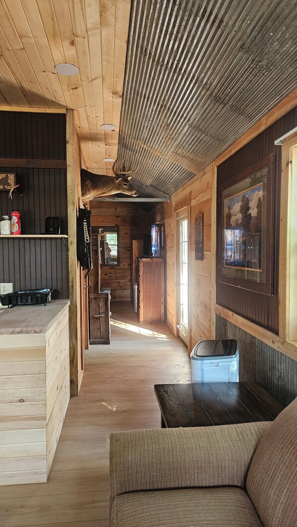 A cabin interior with a wooden floor, a sofa, a table, a kitchen area, and a ceiling fan.
