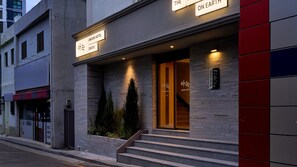 Exterior del Hotel Anook, con fachada moderna, una escalera que lleva a la entrada y un letrero que indica el nombre y la ubicación del hotel.
