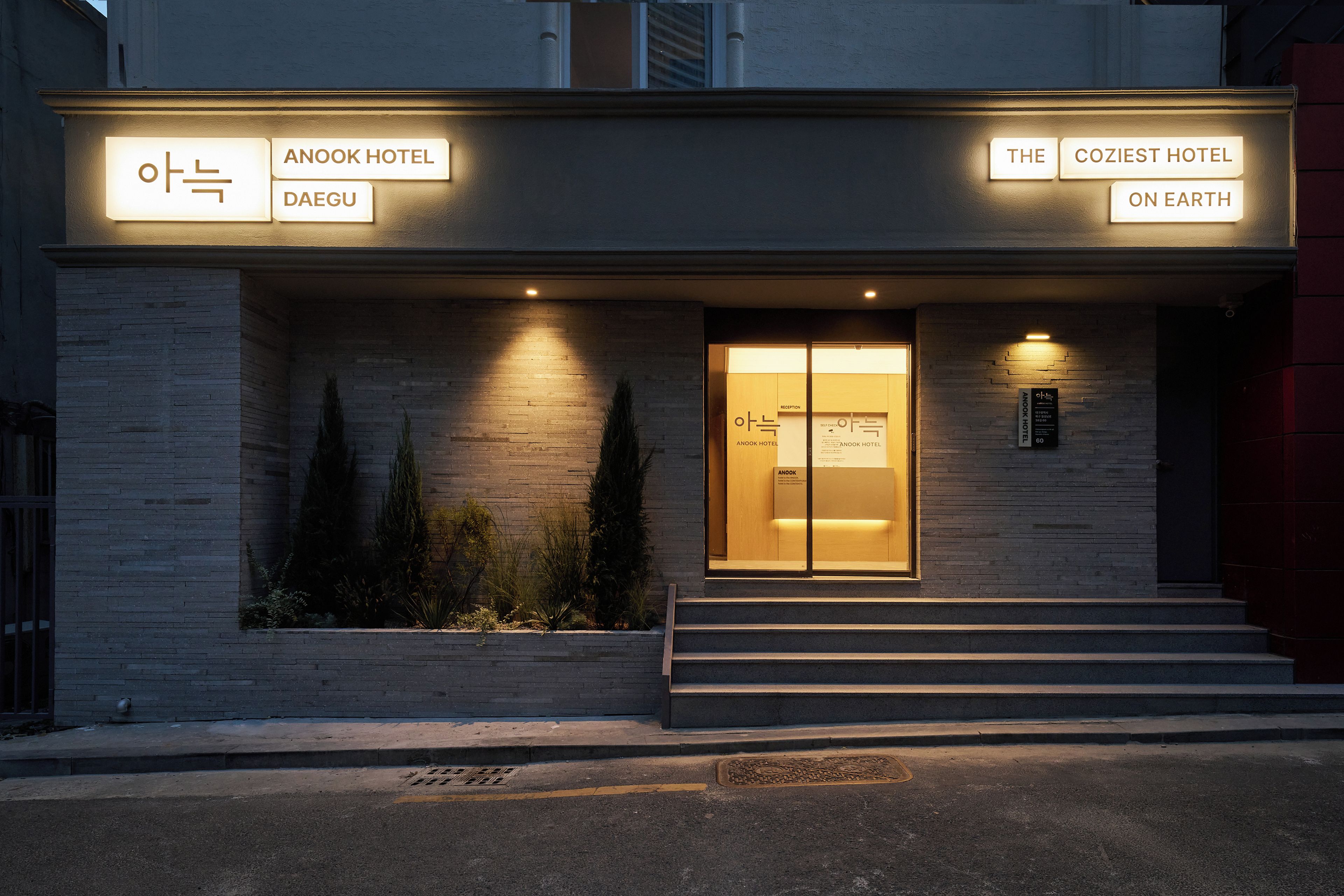 A hotel entrance with illuminated signage for Anook Hotel Daegu and The Coziest Hotel On Earth.