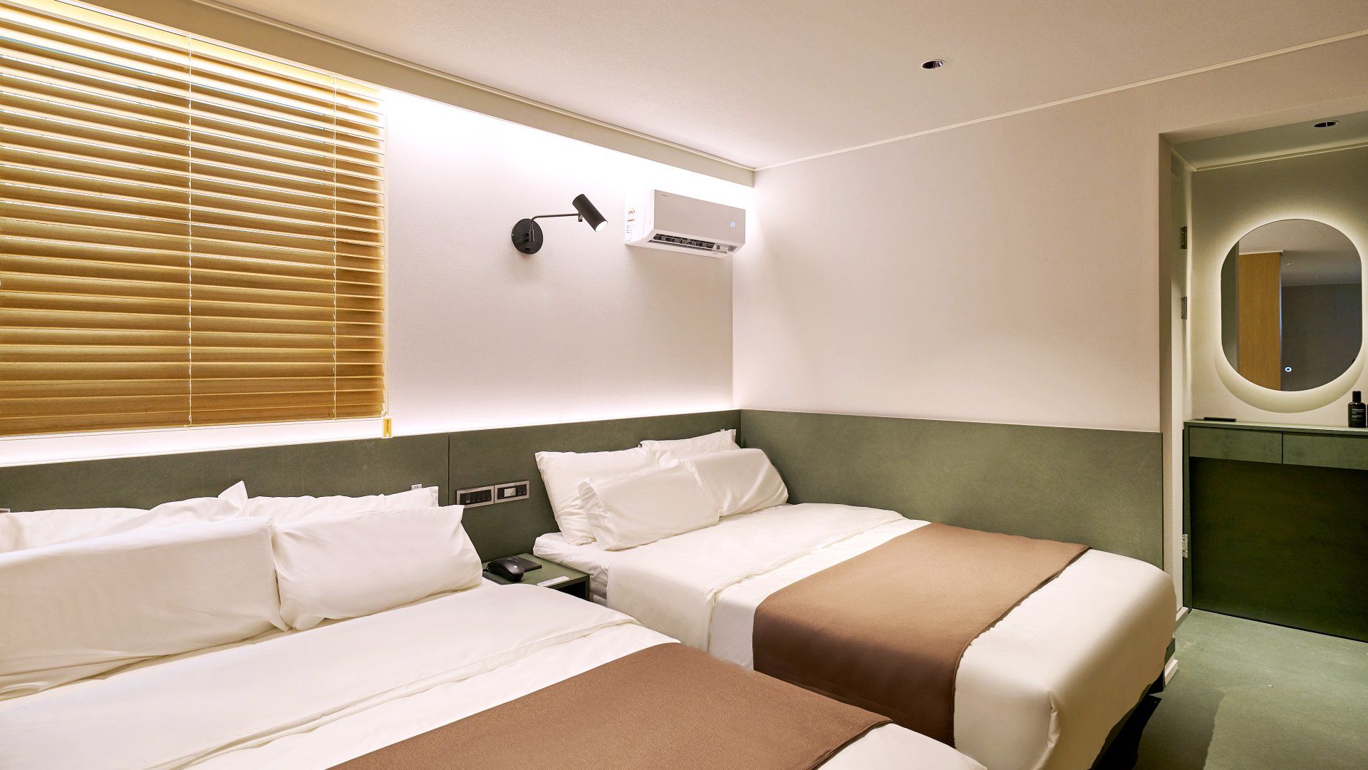 Habitación de hotel con dos camas, una mesita de noche, una lámpara, un equipo de aire acondicionado y un espejo.