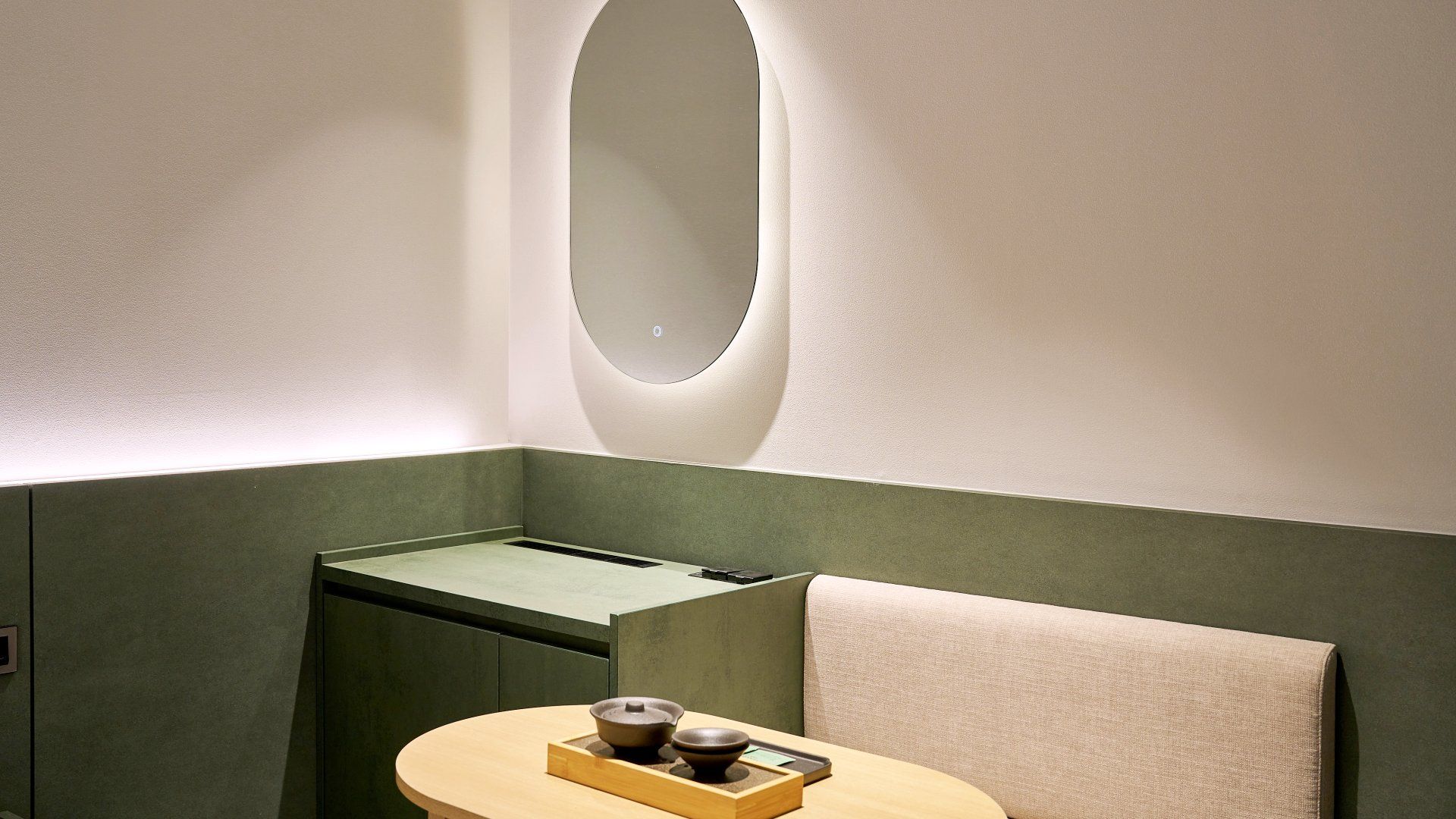 A room with a green accent wall, a round mirror, a small table with a tray, and a towel on a chair.