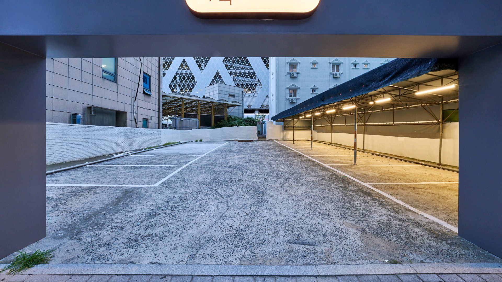 Un estacionamiento exterior con un pasillo cubierto que conduce a un edificio con una fachada geométrica distintiva.