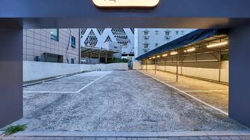 Un estacionamiento exterior con un pasillo cubierto que conduce a un edificio con una fachada geométrica distintiva.