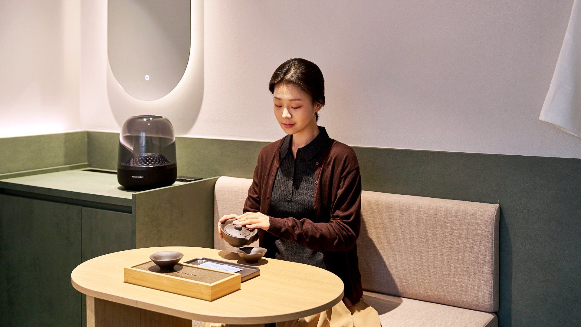 A person seated at a round table with a bowl and a book, in a room with a green accent wall and a modern design.