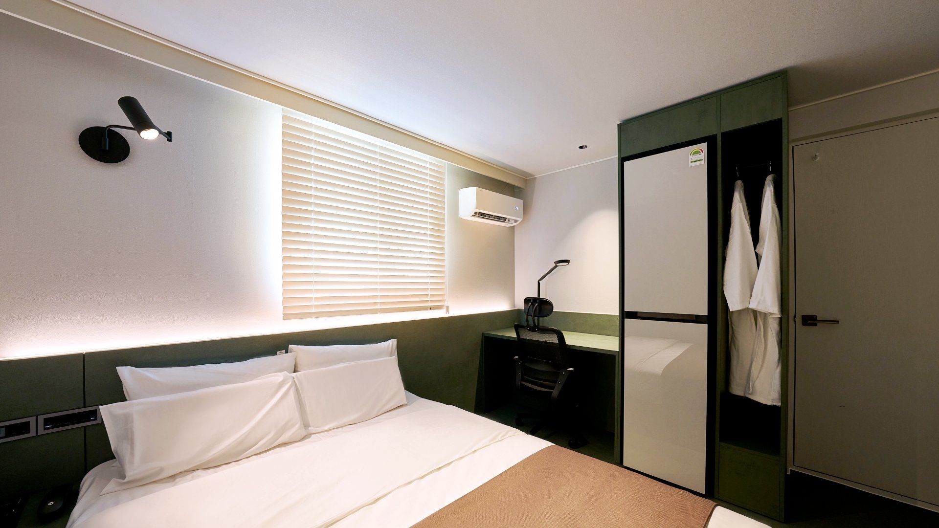 Habitación de hotel con cama, mesita de noche, lámpara, armario y ventana con persianas.
