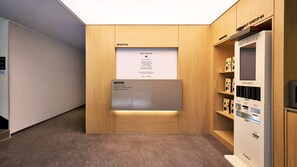 Un área de recepción con mostrador de madera, quiosco de auto-registro y una baraja de cartas.