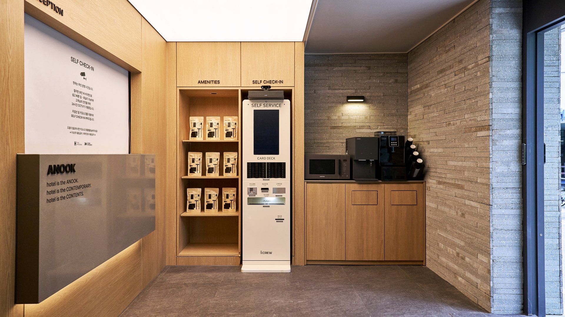 Zona de recepción de hotel con quiosco de autoservicio, zona de servicios y una máquina de café.