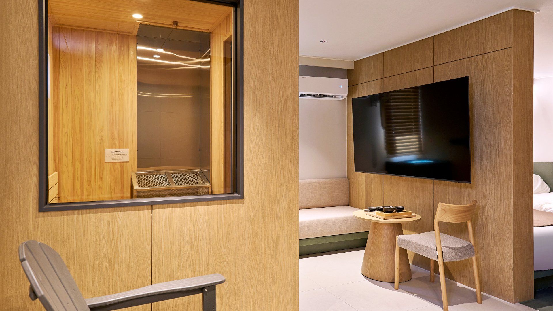 Una habitación moderna con una pared de madera, un televisor de pantalla plana grande, una cama, una mesita redonda con cuencos y una silla.