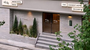 Entrada de hotel con fachada moderna, una escalera que conduce a la entrada, y señalización para Anook Hotel y The Coziest Hotel on Earth.